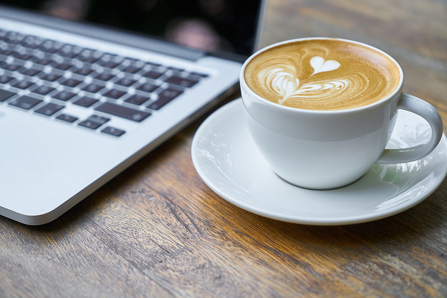 Latte Art Coffee Cup Next to Laptop on Wooden Table