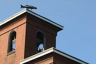 Brick mill tower with fish weathervane against blue sky