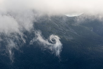 Aerial view of swirling cloud vortex over misty mountain forest
