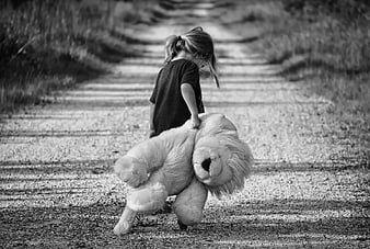 Child dragging large teddy bear down gravel path