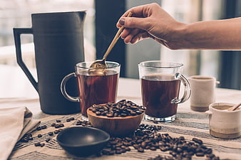 Hand stirring hot coffee in glass mug with beans