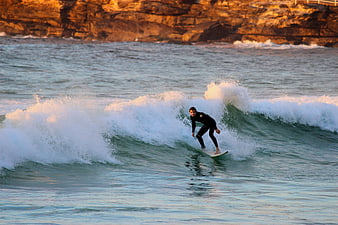 Surfer riding a wave at sunset near rocky cliffs