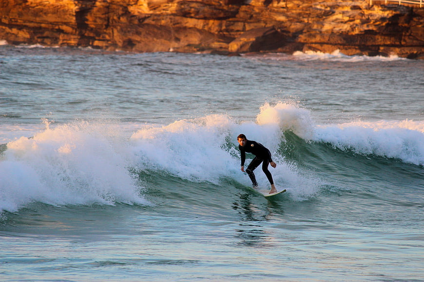 Surfer riding a wave at sunset near rocky cliffs
