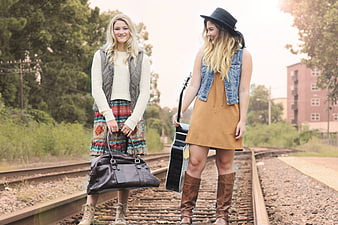 Two young women standing on railroad tracks with guitar and bag