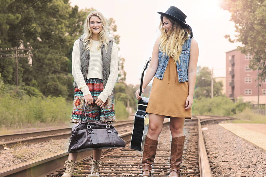 Two young women standing on railroad tracks with guitar and bag