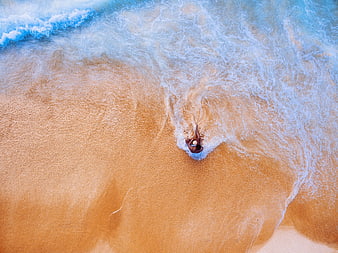 Aerial view of man swimming in ocean waves on sandy beach