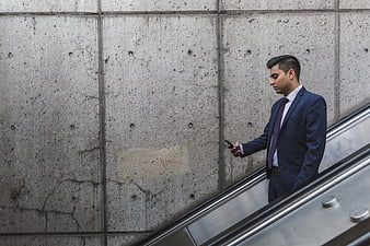 Businessman in Blue Suit Using Smartphone on Escalator