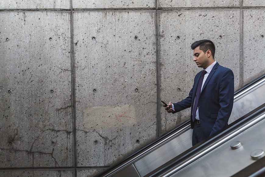 Businessman in Blue Suit Using Smartphone on Escalator