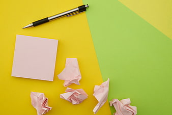 Flat lay of pink sticky notes and pen on yellow and green background