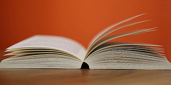 Open book with flipping pages on wooden table against orange background