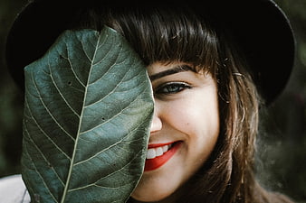 Smiling woman with red lipstick holding a large green leaf