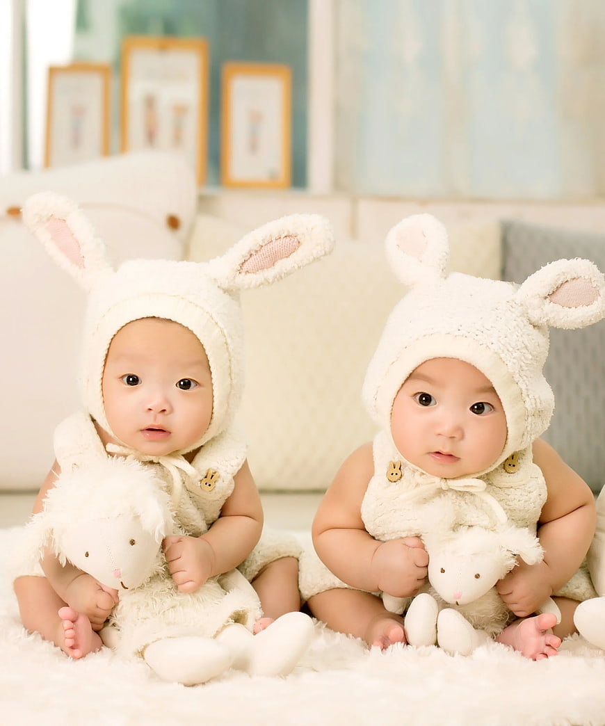 Adorable twin babies in white bunny costumes holding plush toys