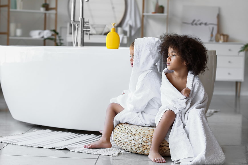 Two children in white bathrobes sitting in a modern bathroom