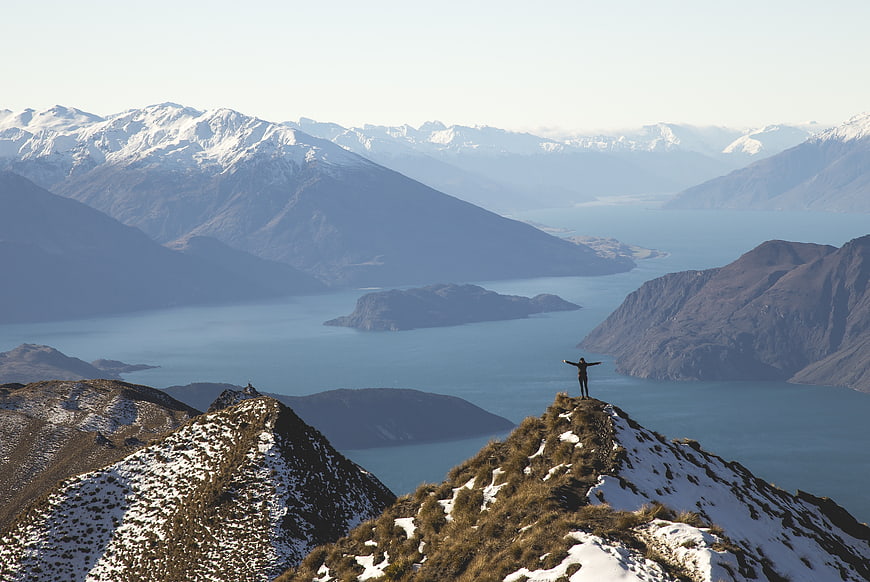 Hiker standing on snowy mountain peak overlooking lake