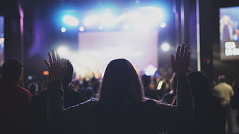 Silhouette of woman raising hands at concert or worship service