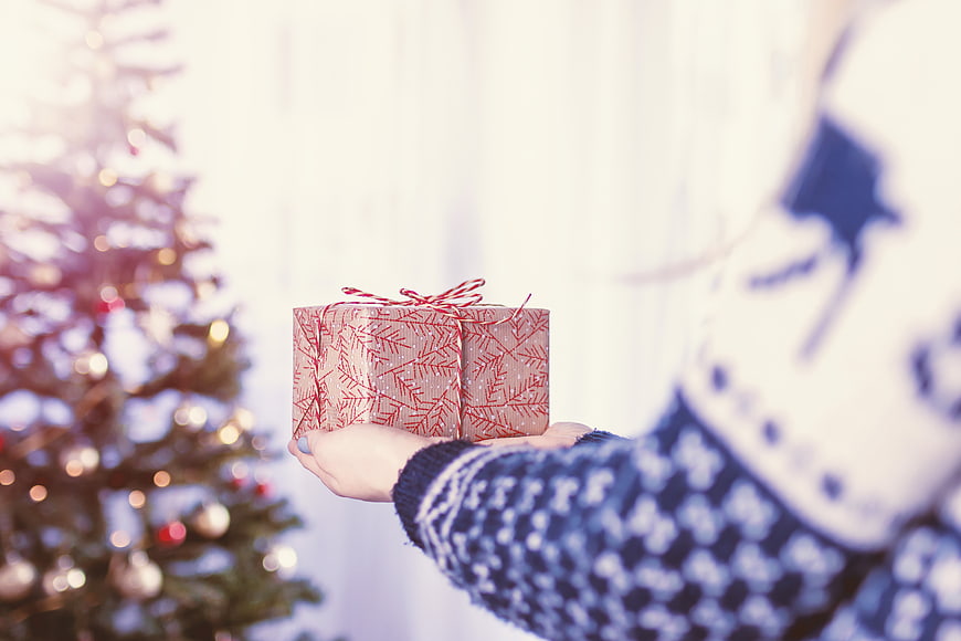 Woman holding Christmas gift box near decorated tree