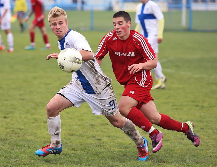 Two young soccer players competing for the ball on a muddy field