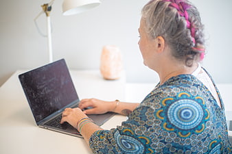 Senior woman with gray hair typing on laptop at white desk