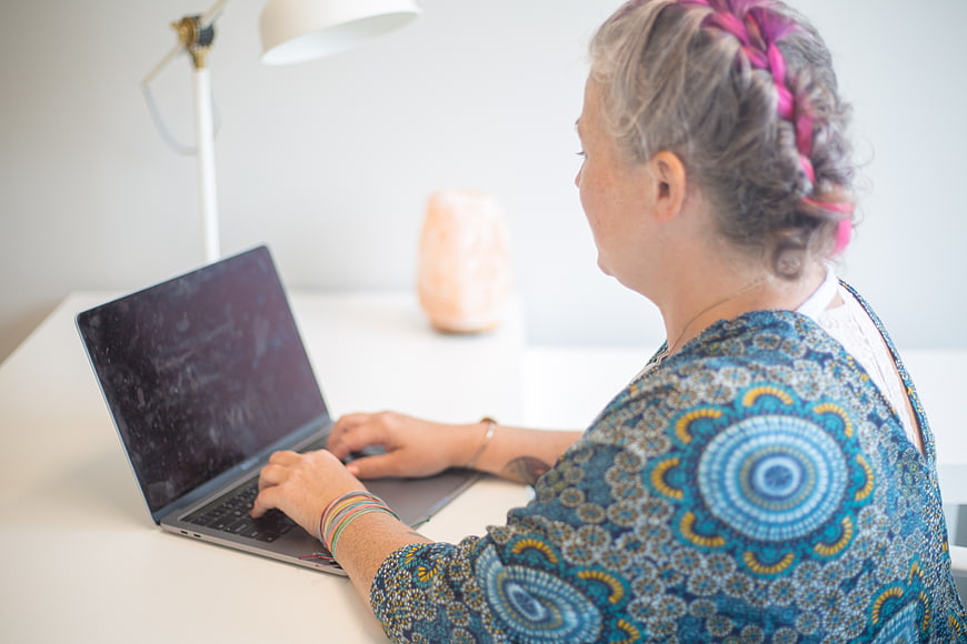 Senior woman with gray hair typing on laptop at white desk