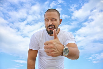 Happy Man Giving Thumbs Up and Winking Against Blue Sky