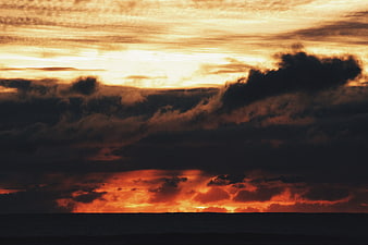 Dramatic sunset over ocean with dark clouds and fiery orange sky