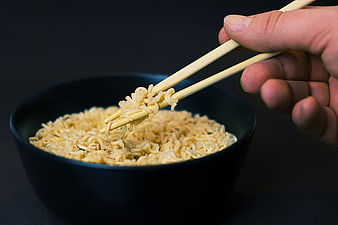 Hand holding chopsticks with instant noodles in a black bowl