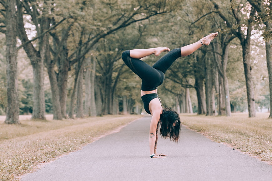 Woman performing advanced yoga handstand in park