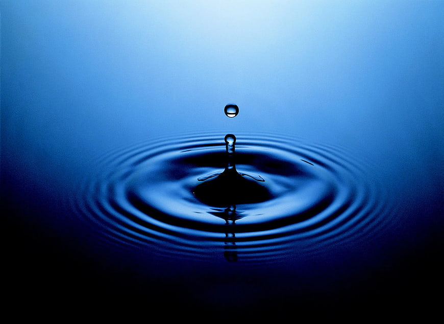 Blue water droplet splash with ripples on dark background