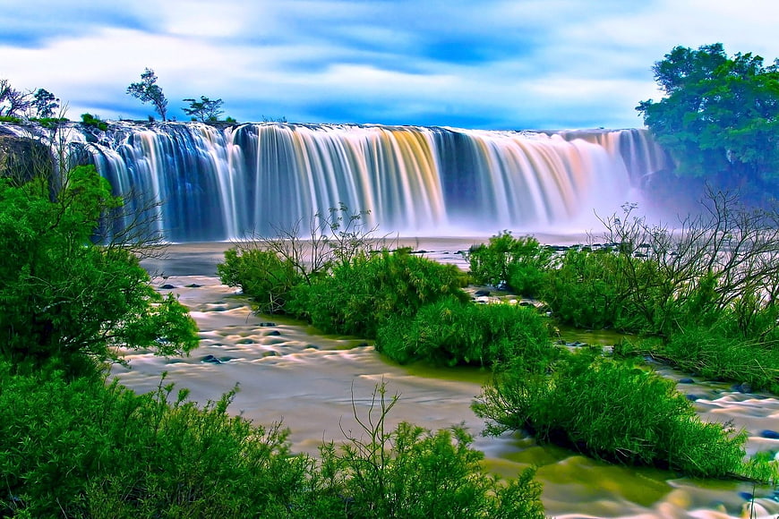 Majestic wide waterfall with lush green vegetation and misty spray