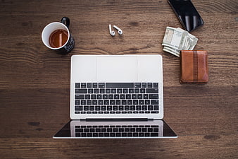 Flat lay of laptop, coffee, wallet, and cash on wooden desk