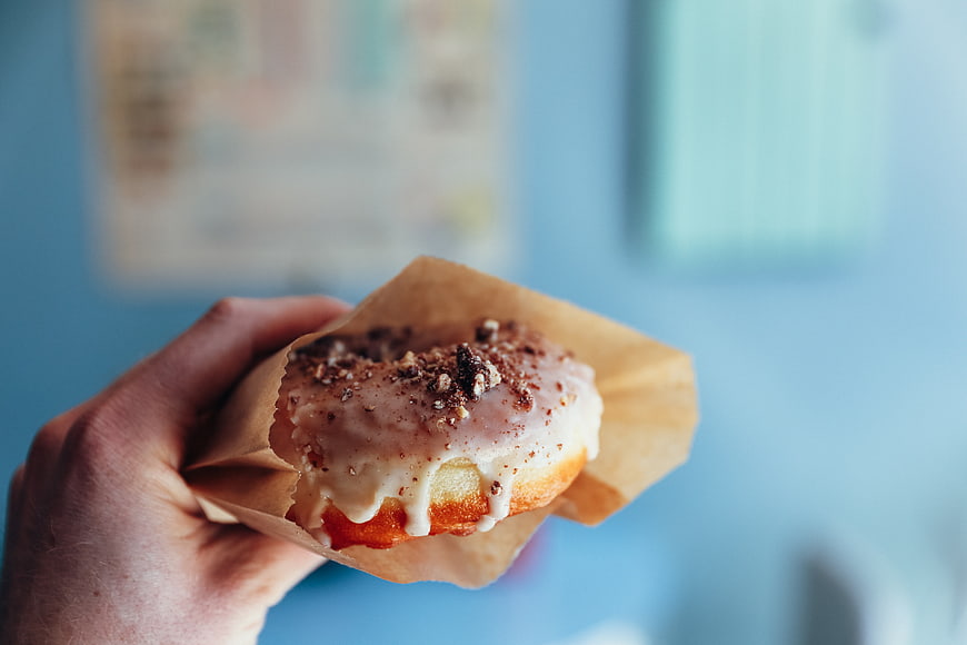 Hand holding glazed donut with crumble topping in brown paper