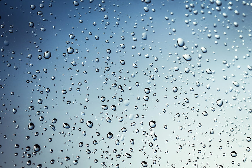 Water droplets on glass against blue sky background