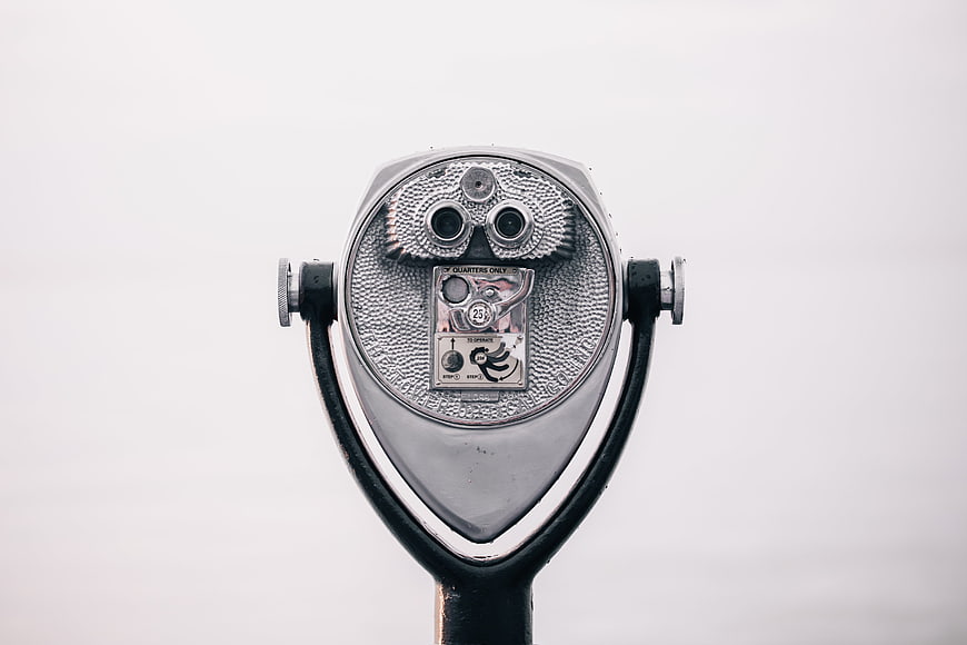 Close-up of silver coin-operated binoculars against white background