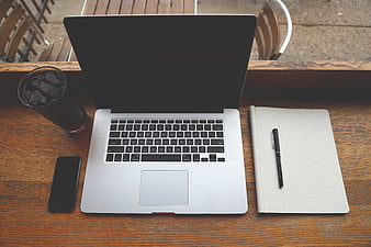 Top-down view of laptop, notebook, and iced coffee on wooden table