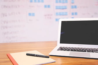 White laptop and notebook on wooden desk with whiteboard background