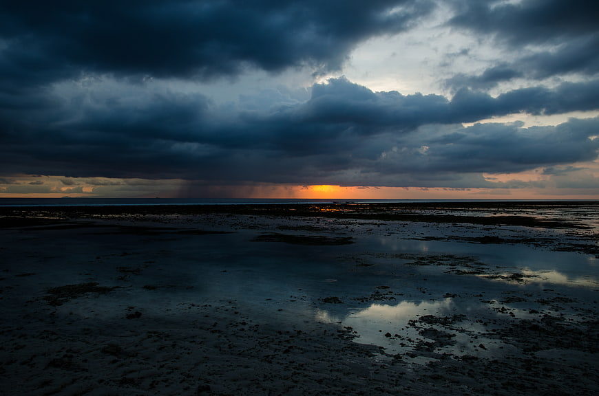 Dramatic stormy sunset over wet tidal flats and ocean horizon