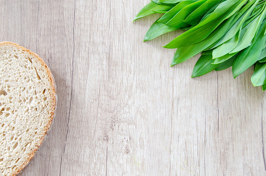 Fresh bread slice and green leaves on wooden background