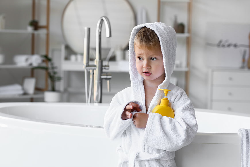 Cute Toddler Boy in White Bathrobe Holding Yellow Soap Bottle