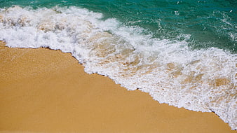 Aerial view of turquoise ocean waves crashing on golden sandy beach