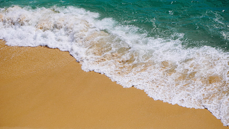 Aerial view of turquoise ocean waves crashing on golden sandy beach
