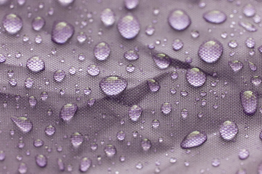 Macro shot of water droplets on purple textured fabric