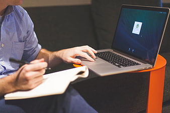 Man Writing Notes While Using Laptop