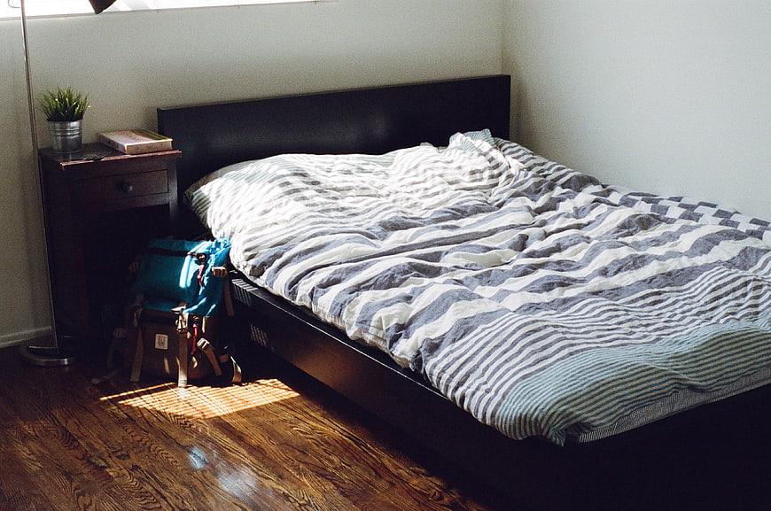 Unmade bed with striped duvet in sunlit bedroom
