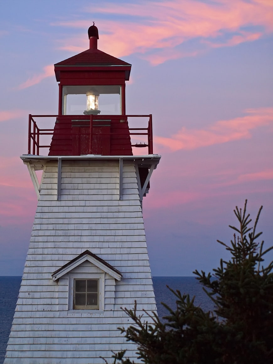 Red and white lighthouse tower against pink sunset sky