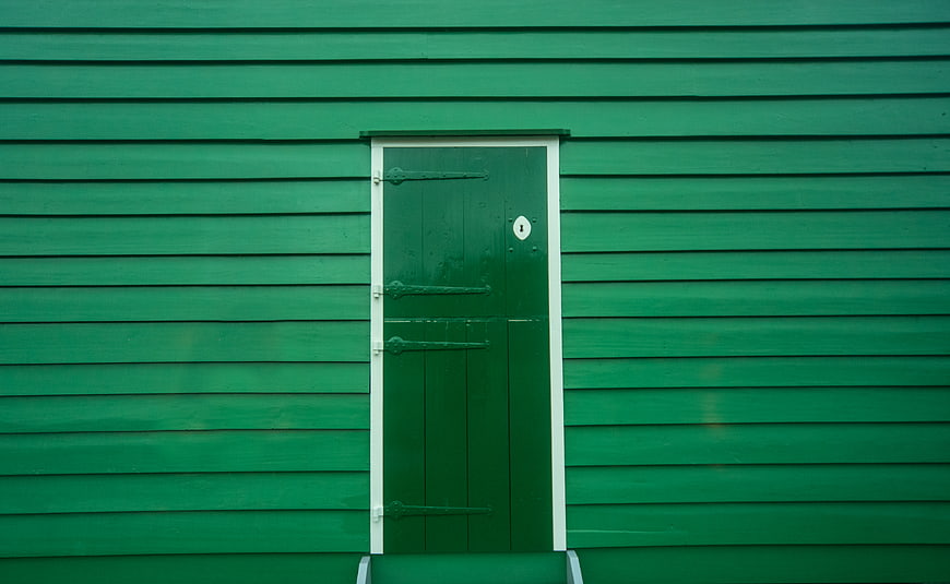 Green wooden door on a green clapboard wall
