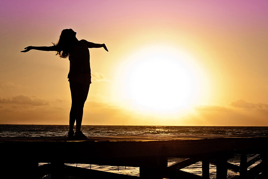 Silhouette of Woman with Arms Outstretched on Pier at Sunset