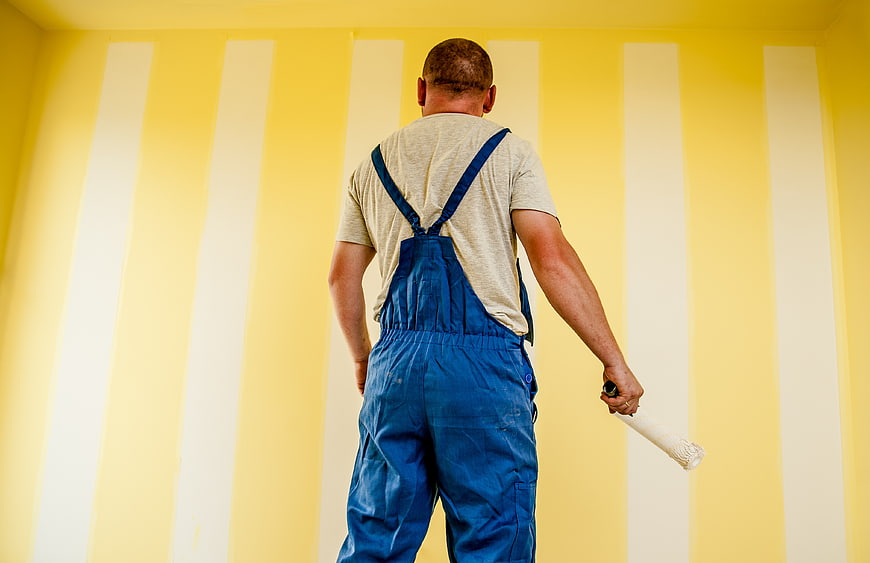 Painter in Blue Overalls Painting Yellow Wall with White Stripes