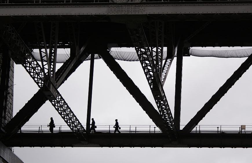 Silhouettes of Pedestrians Walking Under Steel Bridge Truss