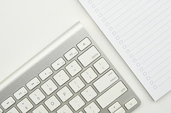 Minimalist silver keyboard and blank checklist paper on white desk