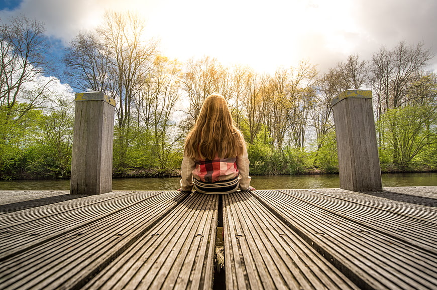 Girl sitting on wooden pier looking at river in spring